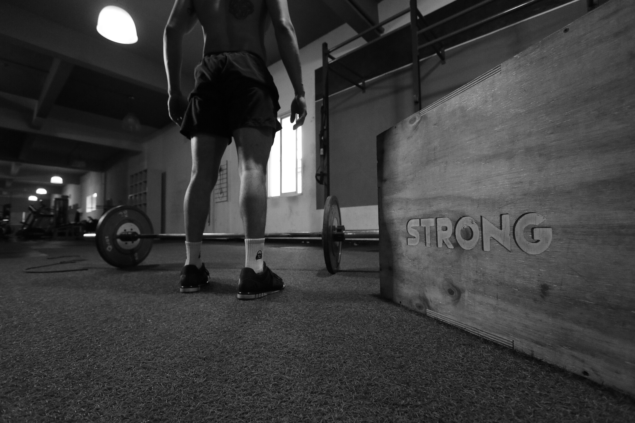 Grayscale Photo Of Man Standing Beside Barbell